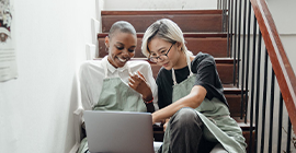 Two people seating on the stairs checking a laptop.